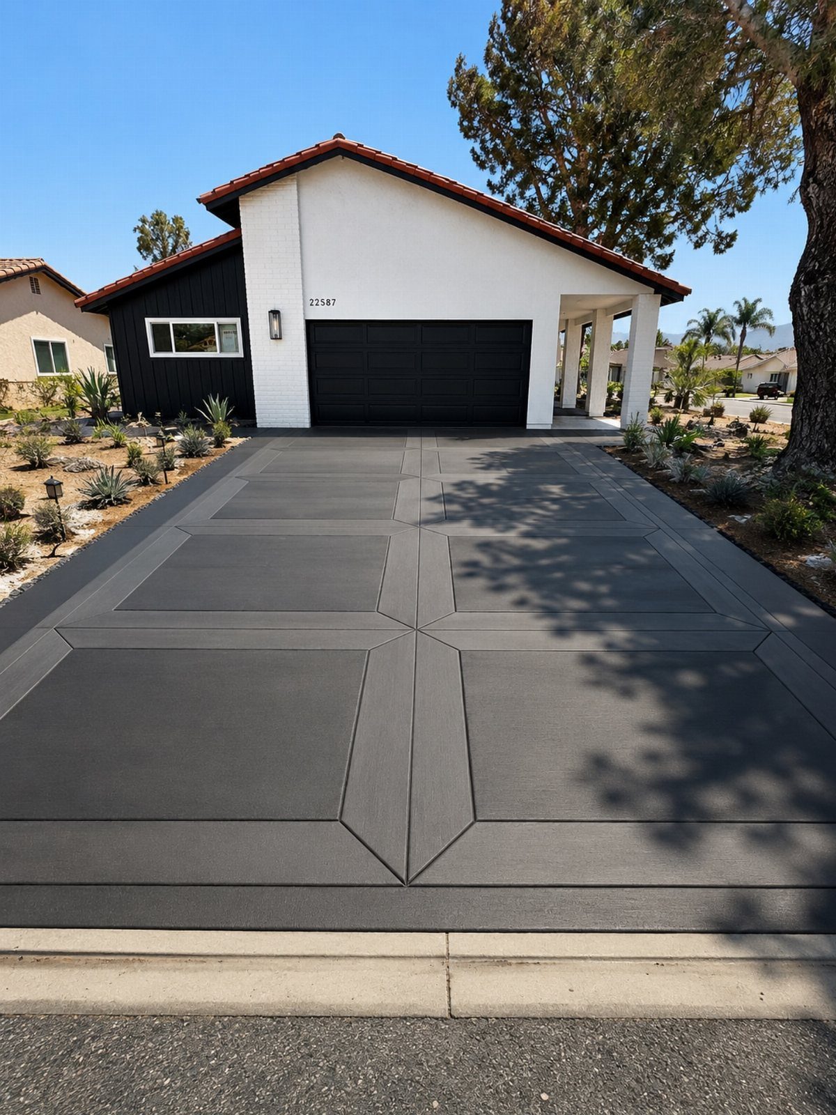 A modern white house featuring a black garage door and a decorative dark grey driveway.