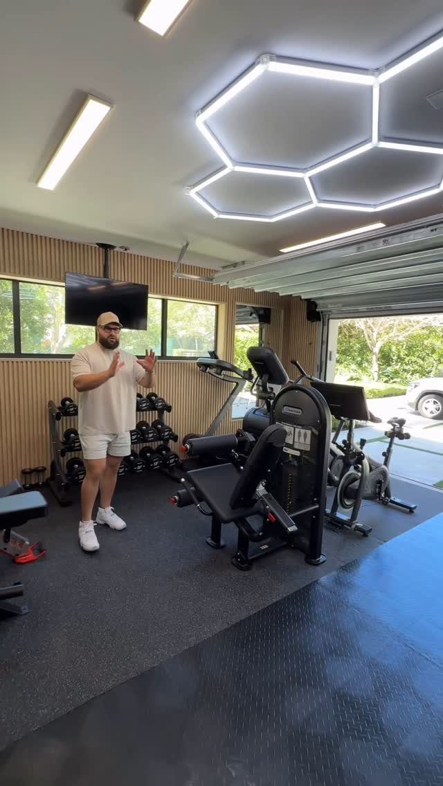 A man standing in a modern garage gym equipped with weight machines and hexagonal LED lights.