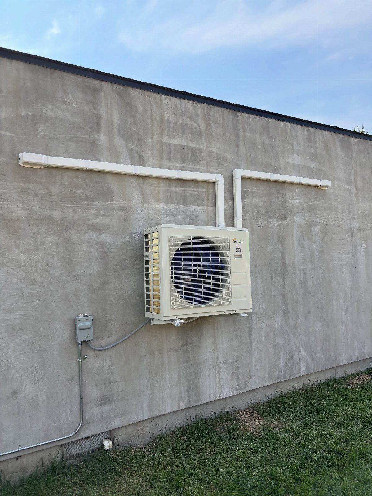White mini-split heat pump condenser unit mounted on a grey concrete wall with white piping.