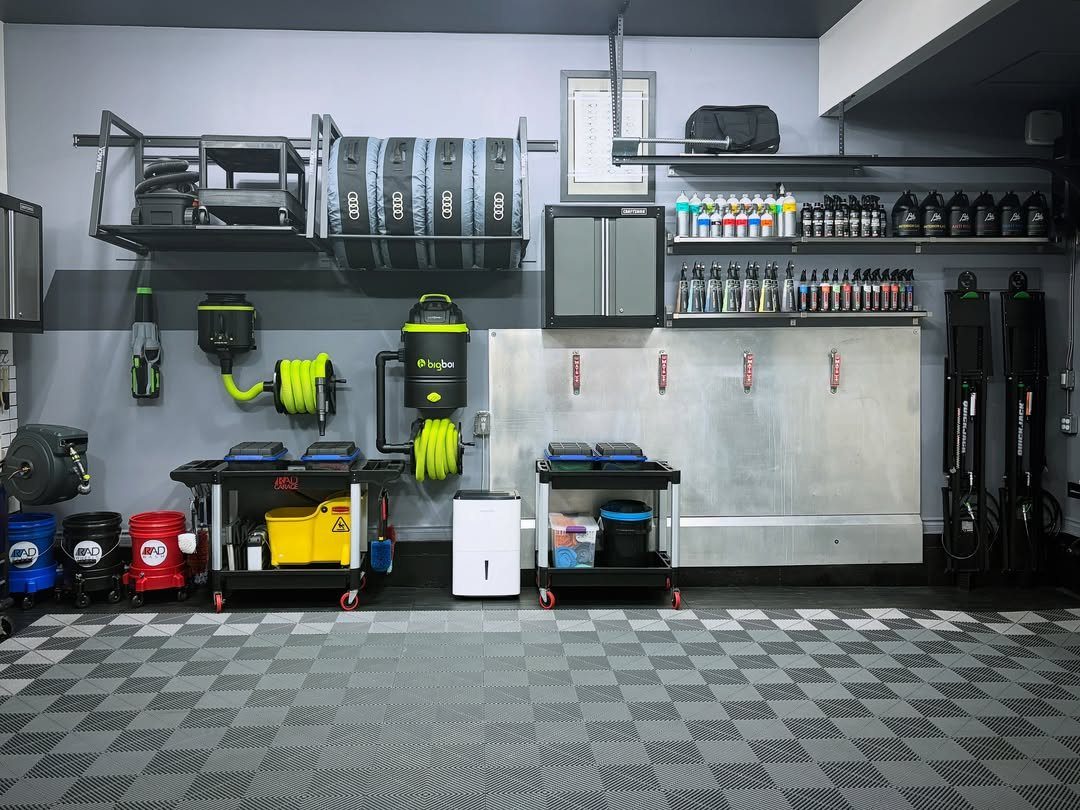 Organized garage interior with cleaning equipment, metal cabinets, and high-mounted storage shelving units.
