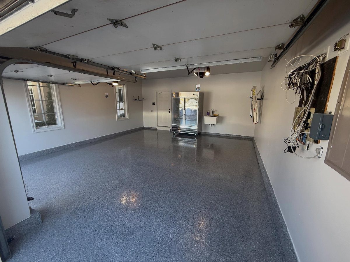 A spacious empty garage with a glossy grey speckled polyaspartic floor coating.