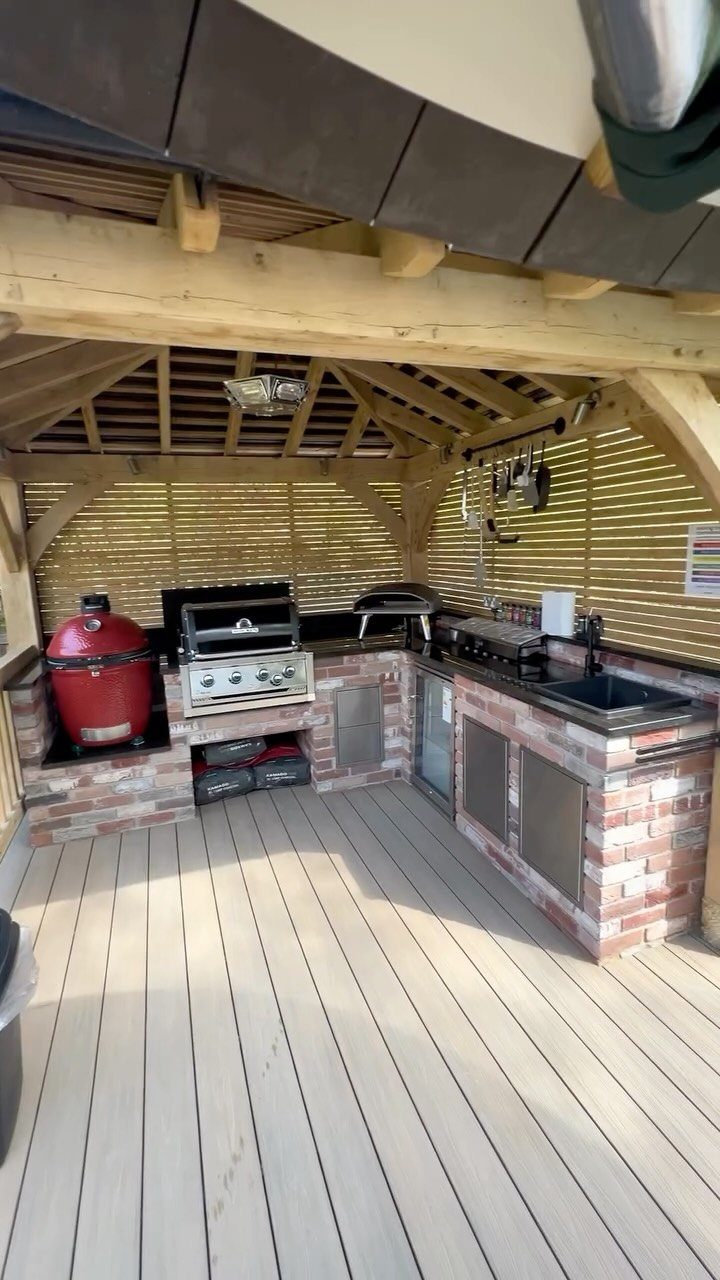Backyard Barbeque Design: 12 BBQ Island Ideas for Outdoor Cooking 5 A brick outdoor kitchen with multiple grills, a sink, and workspaces under a wooden pavilion.