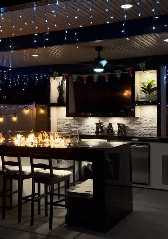 Backyard Barbeque Design: 12 BBQ Island Ideas for Outdoor Cooking 3 Black outdoor kitchen counter with a built-in fire pit and string lights hanging above.