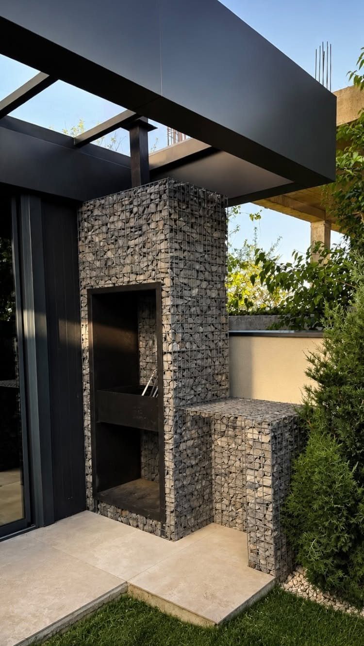 Backyard Barbeque Design: 12 BBQ Island Ideas for Outdoor Cooking 9 A gabion stone structure with a dark metal alcove and stone countertop on a patio.