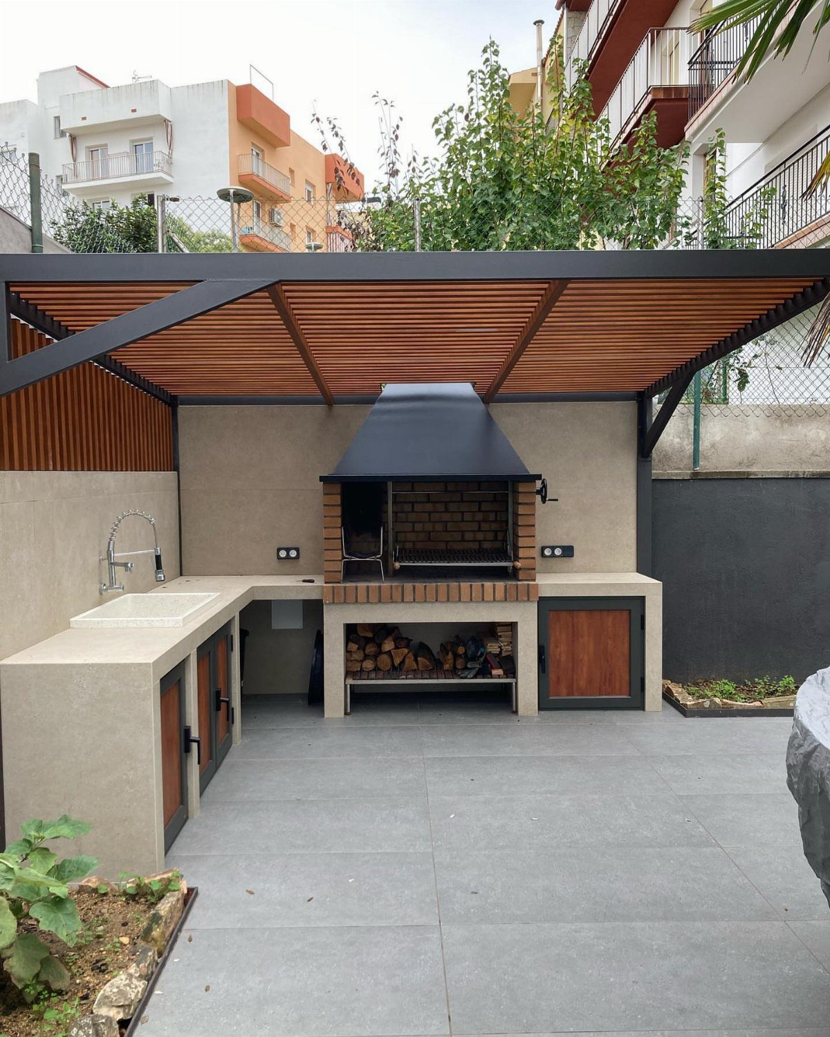 Backyard Barbeque Design: 12 BBQ Island Ideas for Outdoor Cooking 8 Modern outdoor kitchen featuring a stone countertop, built-in sink, and a large wood-fired grill under a pergola.