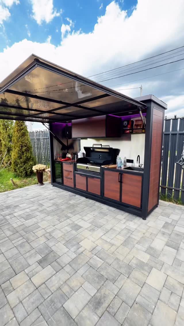 Backyard Barbeque Design: 12 BBQ Island Ideas for Outdoor Cooking 1 A compact outdoor kitchen unit with a retractable canopy, built-in grill, and wood-toned cabinetry on a patio.