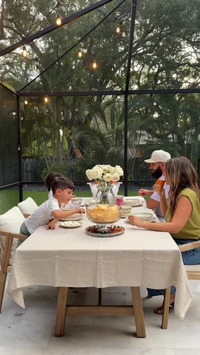 13 Backyard Entertaining Area Ideas for Every Season 6 A family enjoys a meal at a white linen covered table inside a screened patio.
