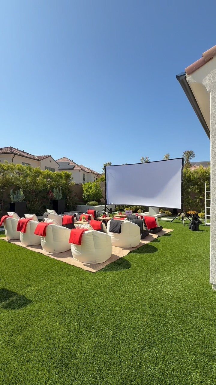 13 Backyard Entertaining Area Ideas for Every Season 11 White projector screen and bean bag chairs arranged on a lawn for an outdoor movie setup.