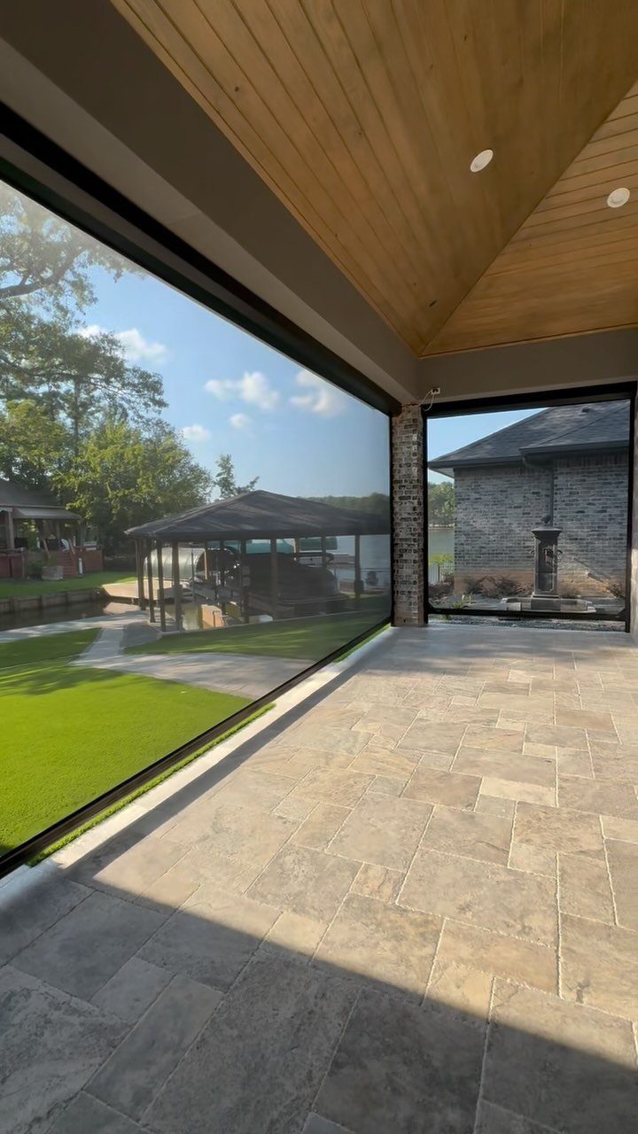 13 Backyard Entertaining Area Ideas for Every Season 7 Retractable screens enclosing a stone patio with a wood ceiling overlooking a green yard.