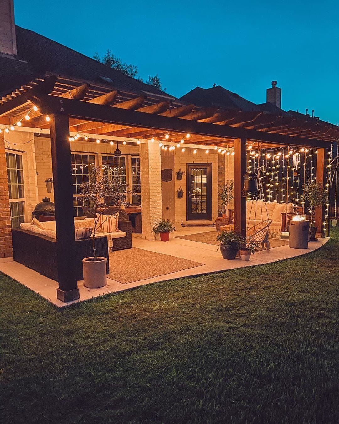 13 Backyard Entertaining Area Ideas for Every Season 5 String lights hanging from a dark wooden pergola over a cozy outdoor patio seating area.