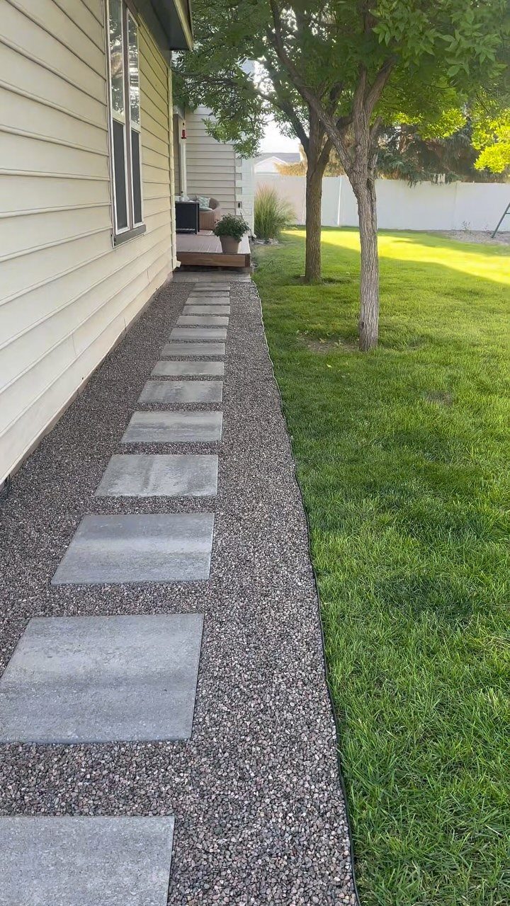 Grey stone pavers set into a gravel walkway running alongside a house and green lawn.
