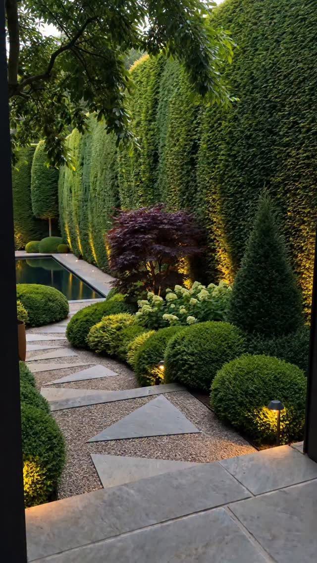 Tall manicured green hedges line a landscaped garden with shaped shrubs and stone pathways.