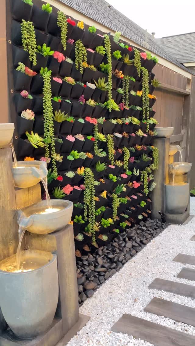 A vertical garden wall featuring many colorful succulents in black fabric pockets between stone fountains.
