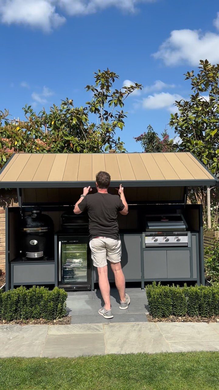 A man standing before a modern built-in outdoor kitchen with a stainless steel grill.