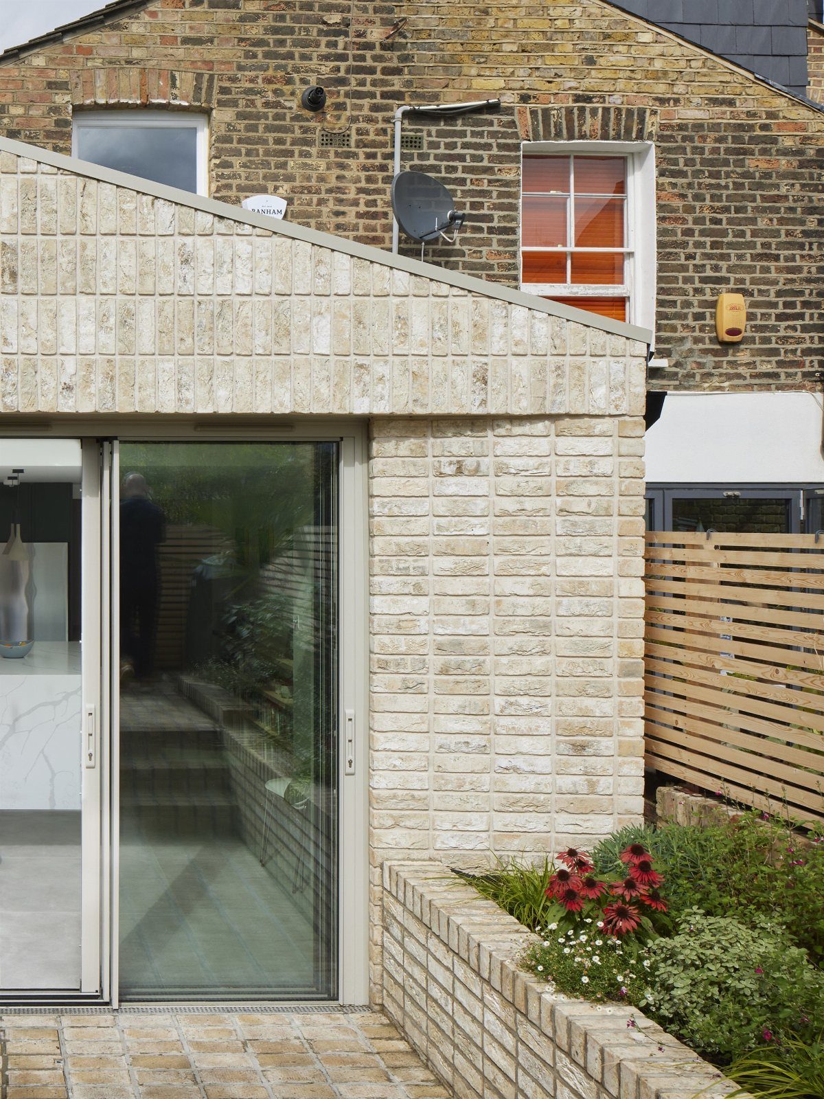 Light brick building extension with a sliding glass door and a small brick patio area.