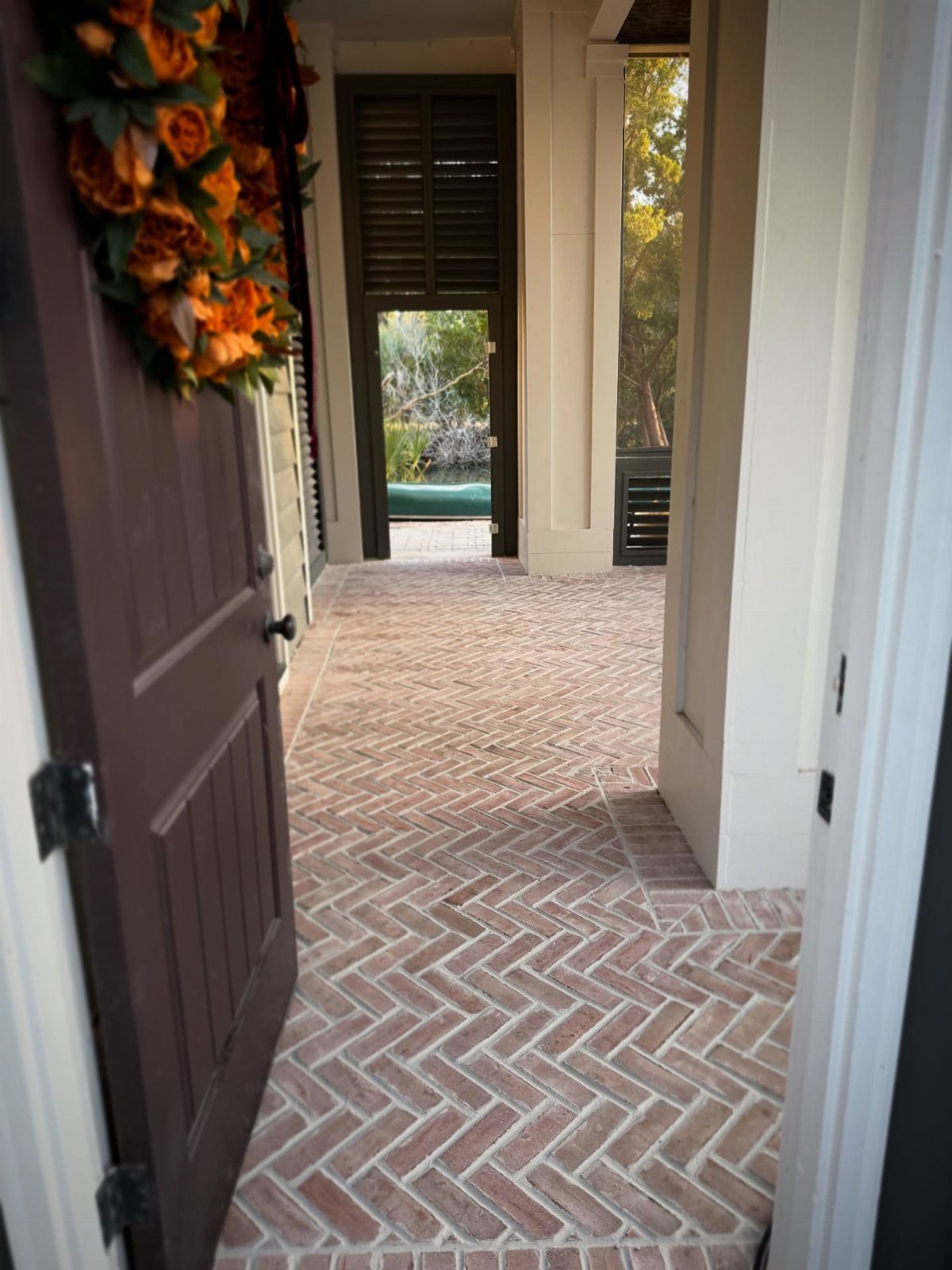 Red and tan bricks laid in a herringbone pattern on a narrow outdoor porch walkway.