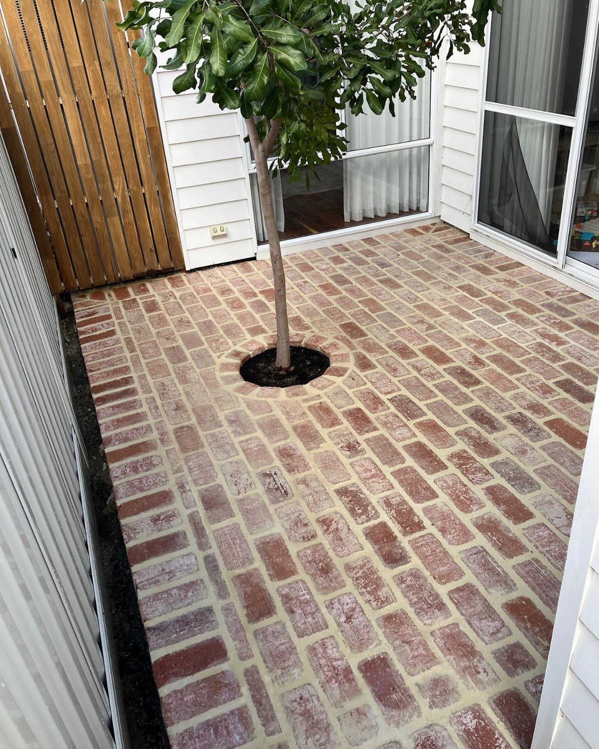 Reddish-brown bricks laid in a running bond pattern around a small tree in a patio.