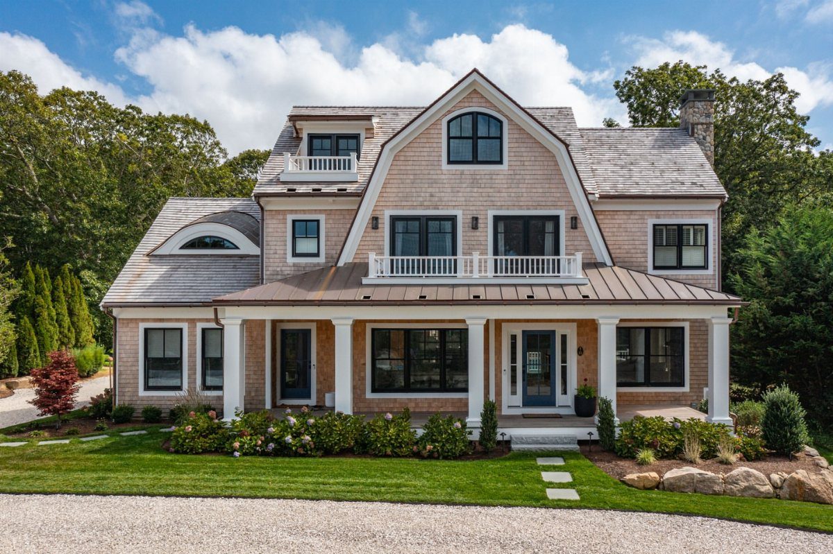 9 Cape Cod House Exterior Ideas for Curb Appeal 6 A large shingle-sided Cape Cod house with white columns and a wide front porch.