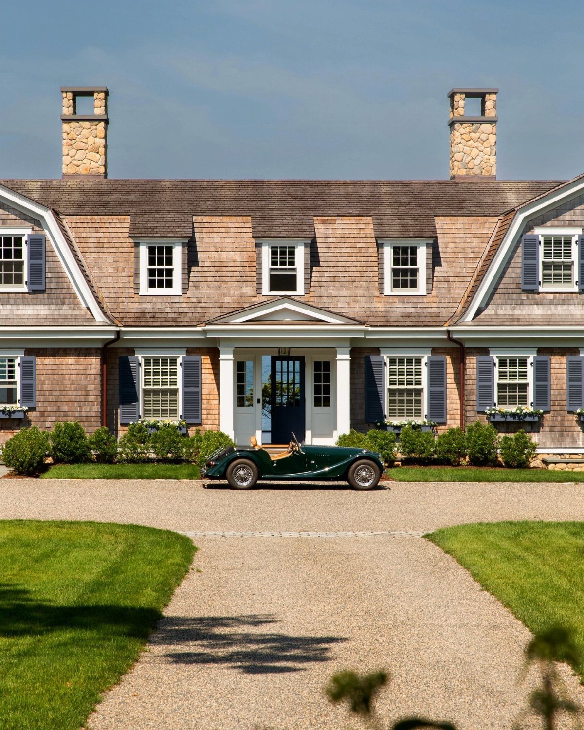 9 Cape Cod House Exterior Ideas for Curb Appeal 8 Symmetrical Cape Cod house with shingled roof, dormers, and blue shutters featuring a vintage car.