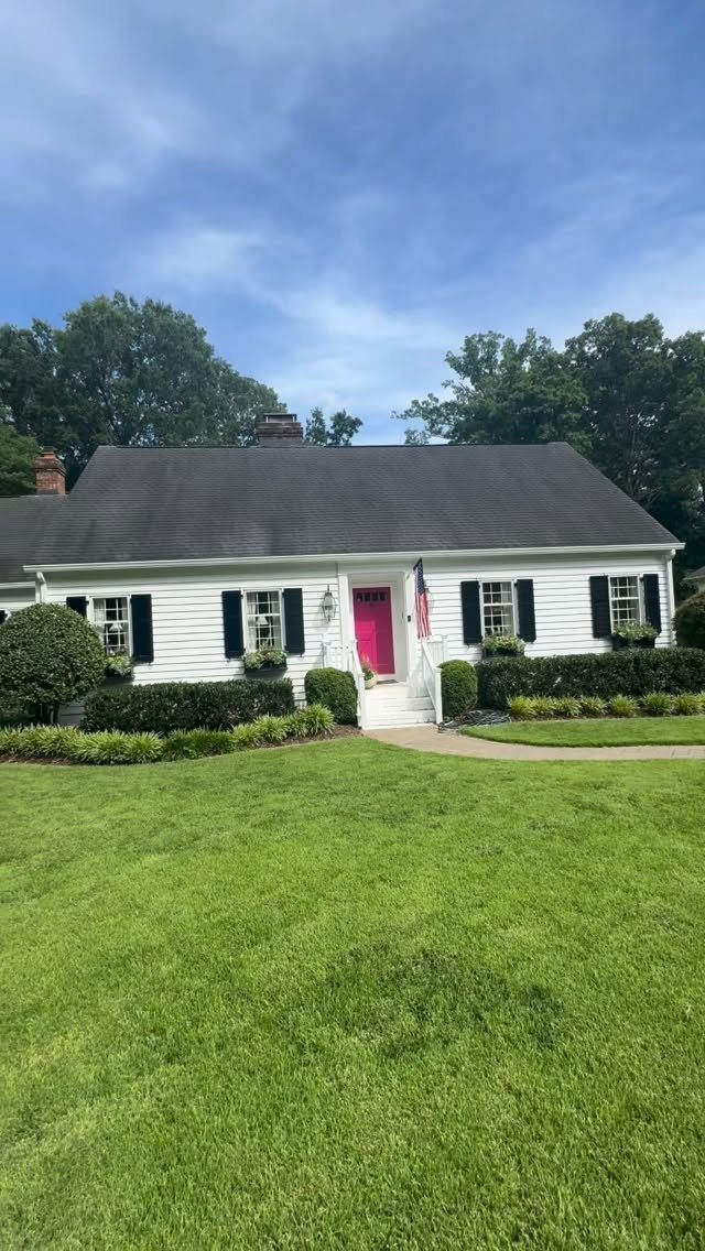 9 Cape Cod House Exterior Ideas for Curb Appeal 4 A white Cape Cod house featuring black shutters and a vibrant pink front door.