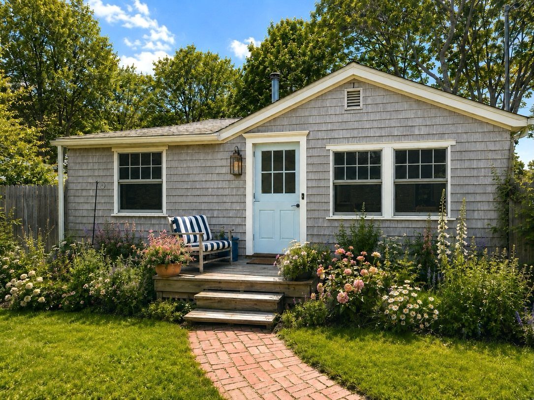 9 Cape Cod House Exterior Ideas for Curb Appeal 7 Grey shingle cottage with a light blue door, white trim, and colorful flower gardens in front.