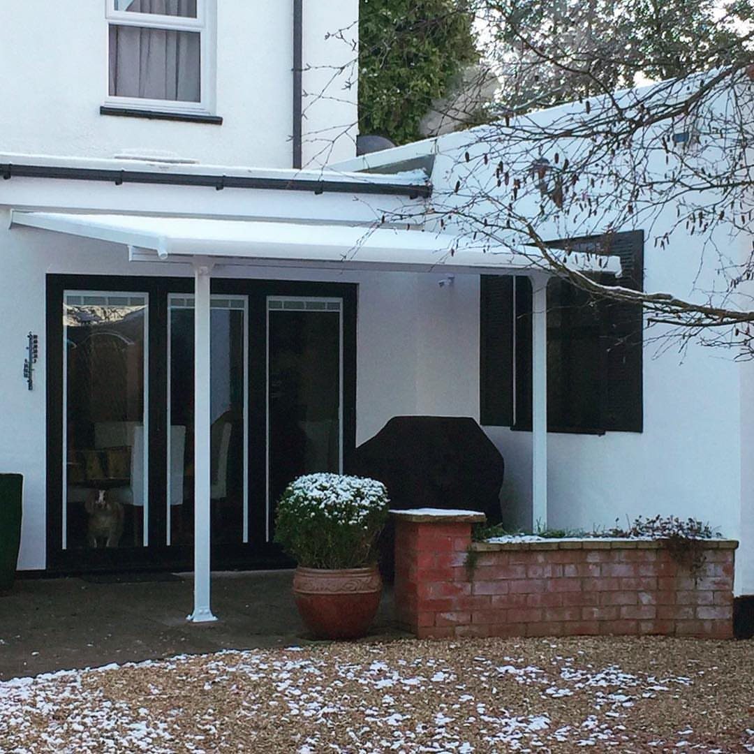 20 Covered Patio Ideas for Shade, Style and Year-Round Use 16 A white retractable awning provides shade over a patio area next to a white house.