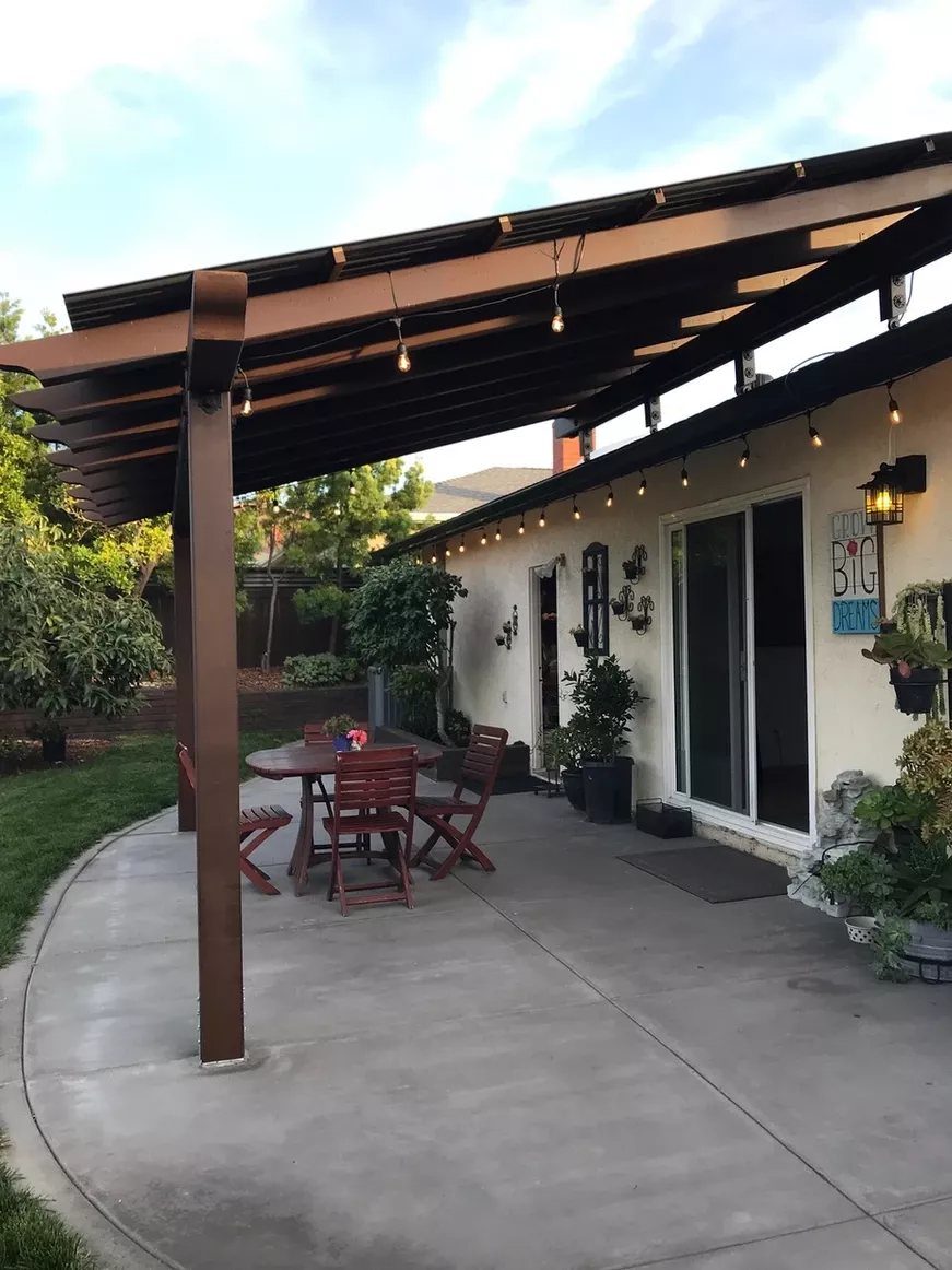 20 Covered Patio Ideas for Shade, Style and Year-Round Use 3 Metal roof patio cover over a concrete patio with a wooden dining set.