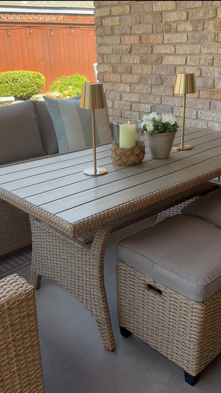 20 Covered Patio Ideas for Shade, Style and Year-Round Use 15 A wicker dining table with grey cushions, gold lamps, and a candle on a patio.