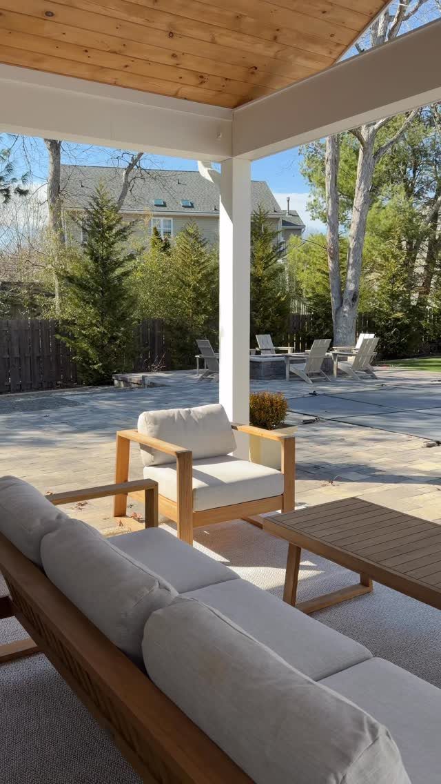 20 Covered Patio Ideas for Shade, Style and Year-Round Use 12 Wooden outdoor lounge furniture with grey cushions sits on a grey rug under a wooden ceiling.