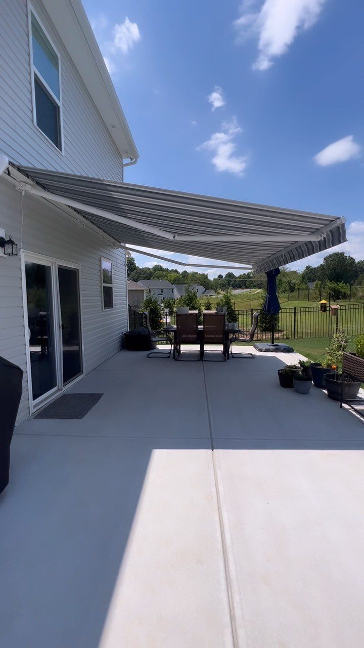 20 Covered Patio Ideas for Shade, Style and Year-Round Use 2 A grey retractable awning provides shade over a concrete patio and outdoor dining set.