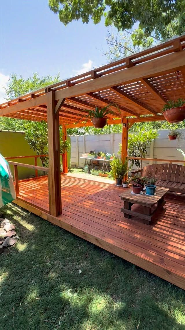 20 Covered Patio Ideas for Shade, Style and Year-Round Use 1 A wooden deck with a pergola, small table, and bench in a backyard.