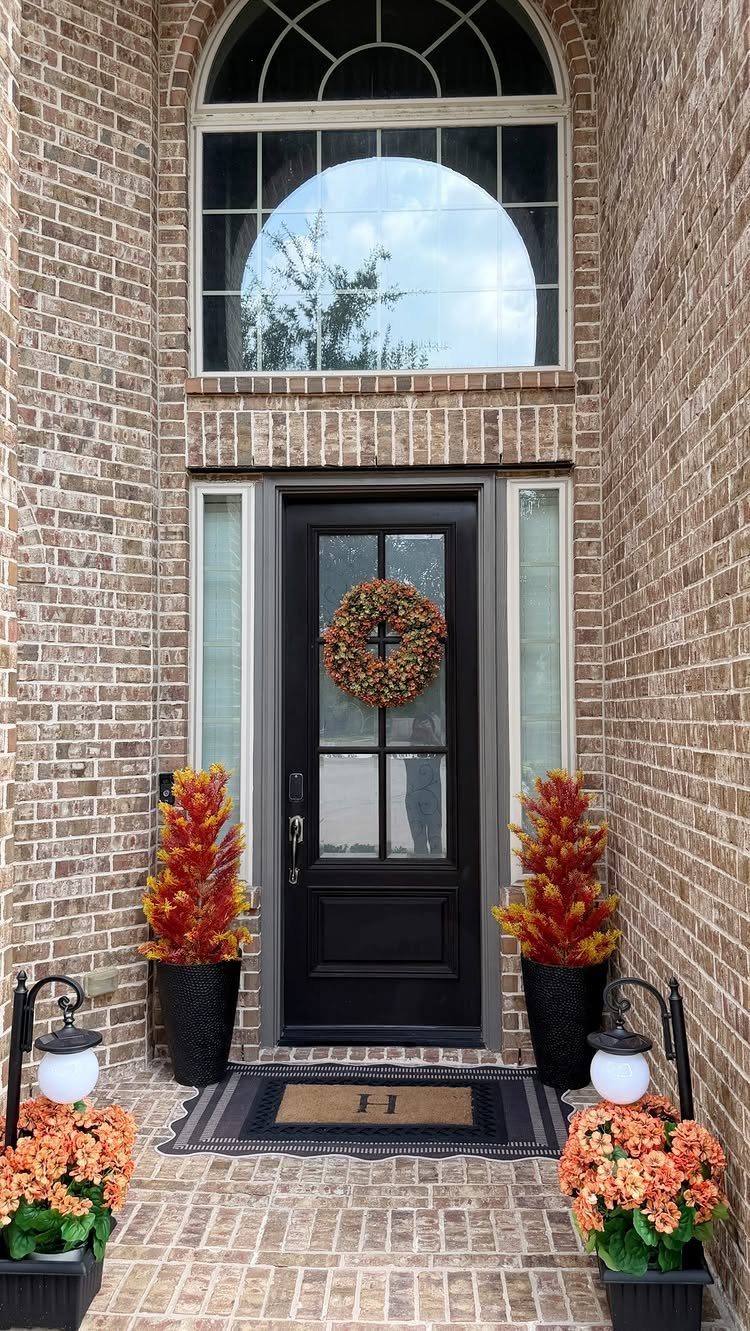 10 Curb Appeal Ideas for a Sharper Front Facade in 2026 7 Black front door decorated with a wreath and surrounded by orange seasonal plants in black planters.