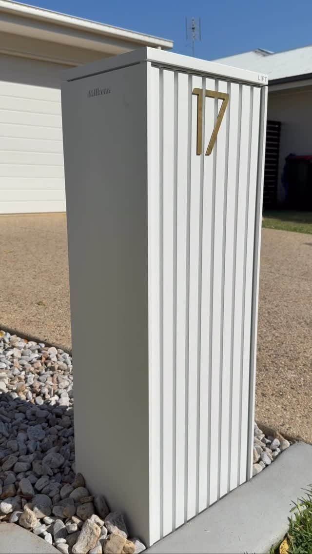 10 Curb Appeal Ideas for a Sharper Front Facade in 2026 1 A modern grey ribbed mailbox pillar with gold number 17 stands among decorative stones.