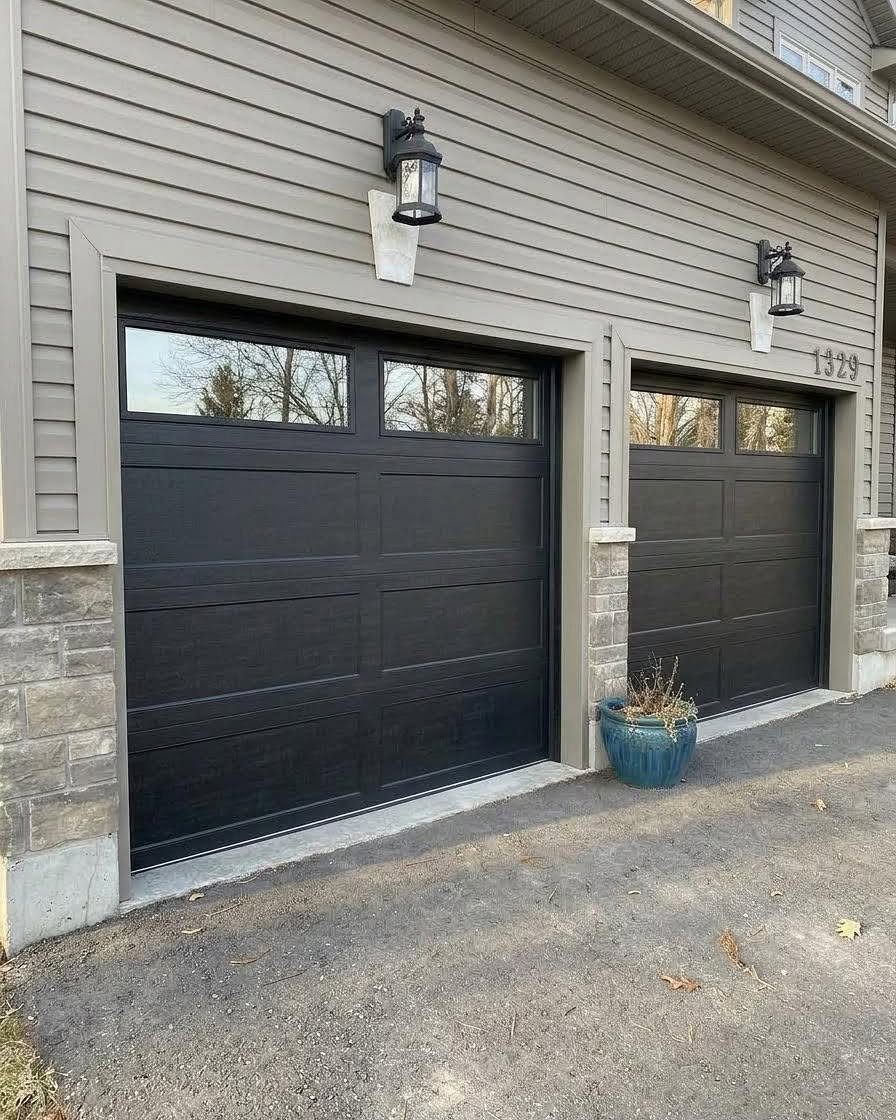 10 Curb Appeal Ideas for a Sharper Front Facade in 2026 5 Two black garage doors set into grey siding with stone accents and outdoor wall lanterns.