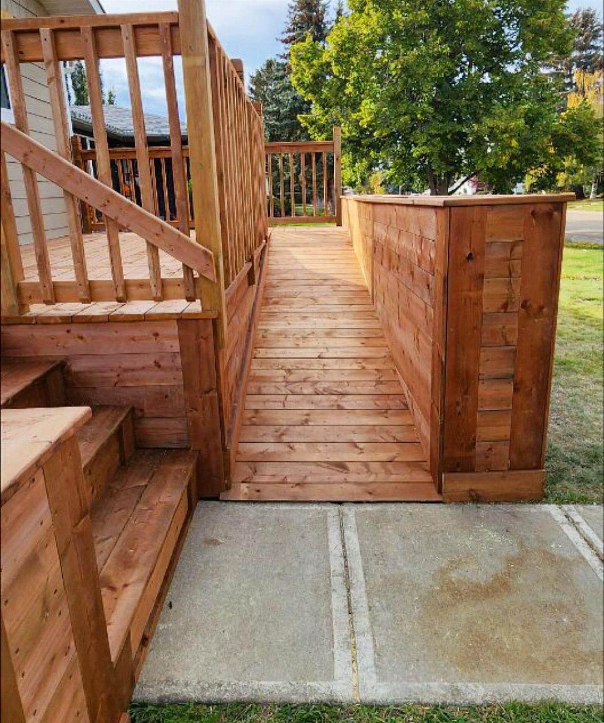 4 Deck Ramp Ideas for Every Yard and Budget 1 A wooden deck ramp constructed from light brown planks connecting a concrete path to a raised deck.