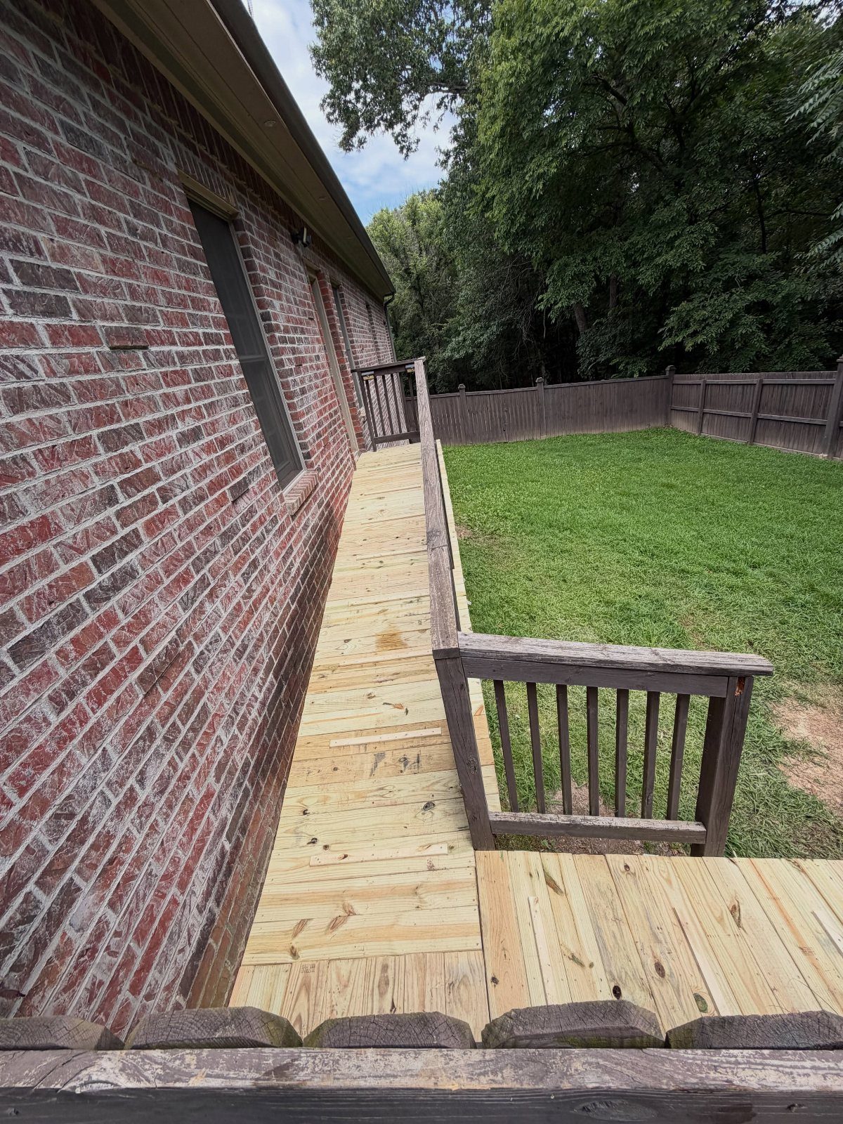 4 Deck Ramp Ideas for Every Yard and Budget 4 A long wooden ramp constructed alongside a brick house leading to a grassy backyard.