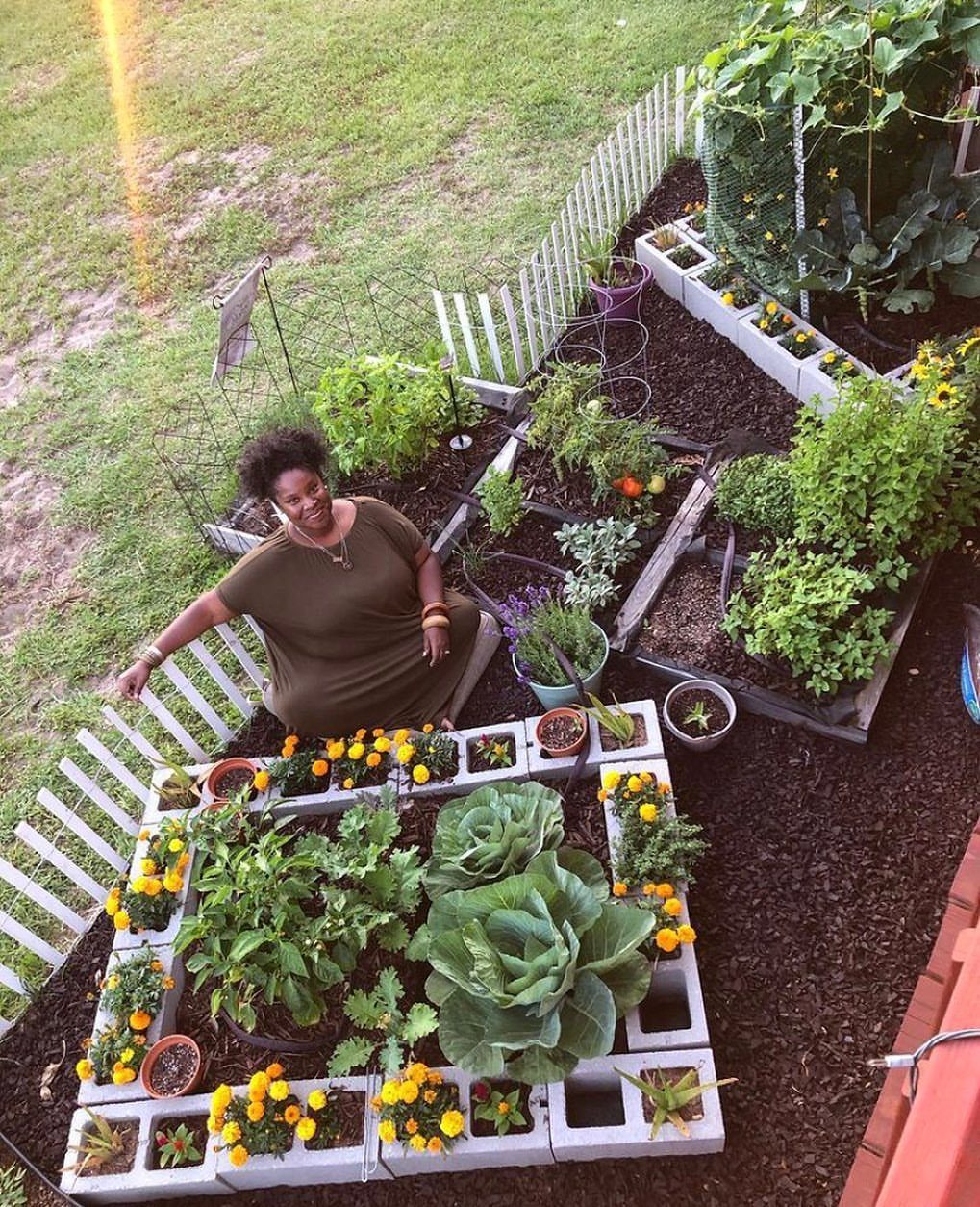 Easy Raised Garden Beds with 8 Material Ideas 4 A woman sitting in a garden next to raised beds made of cinder blocks.