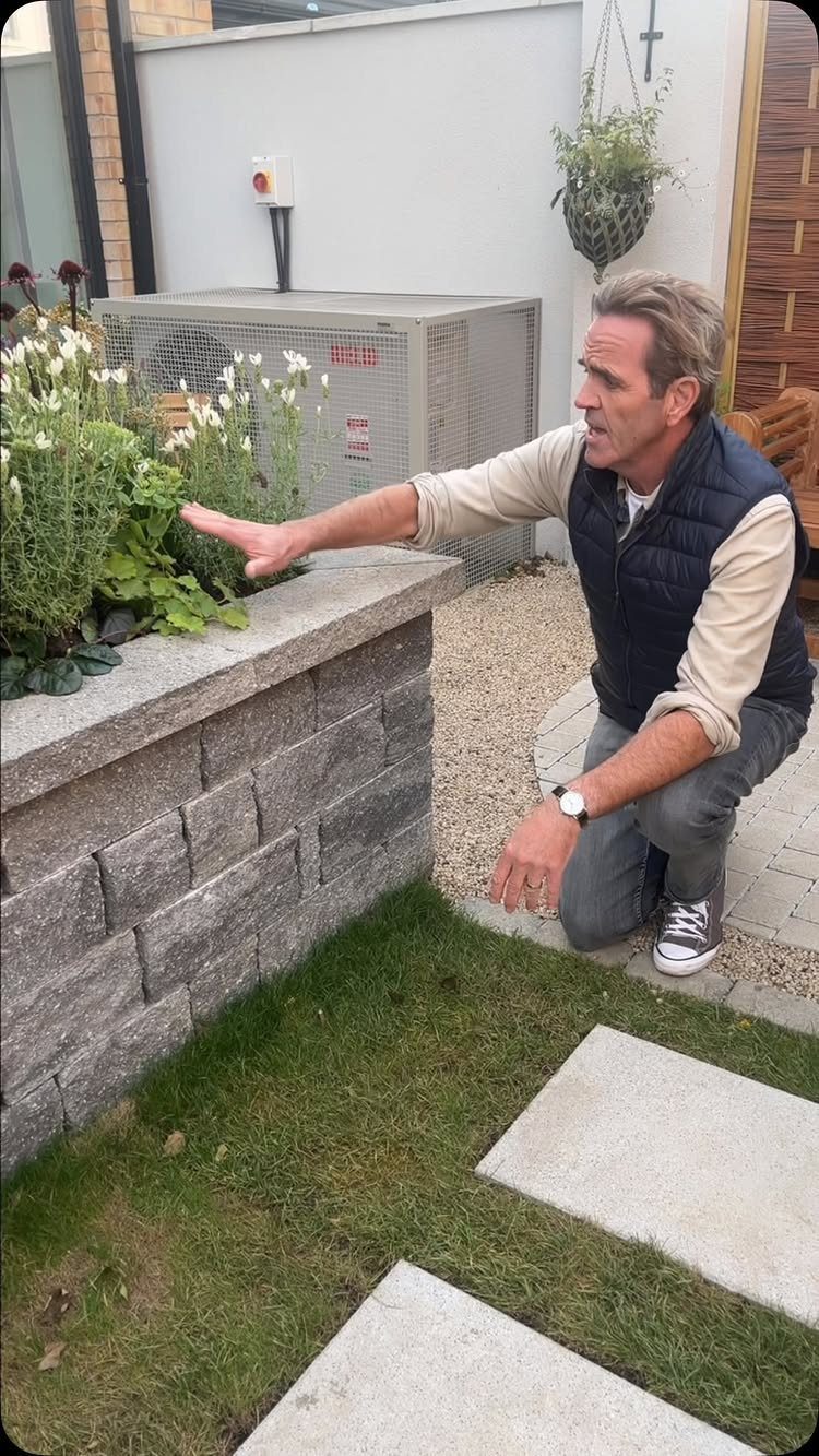 Easy Raised Garden Beds with 8 Material Ideas 5 A man kneeling beside a grey stone raised garden bed containing white flowers and green foliage.