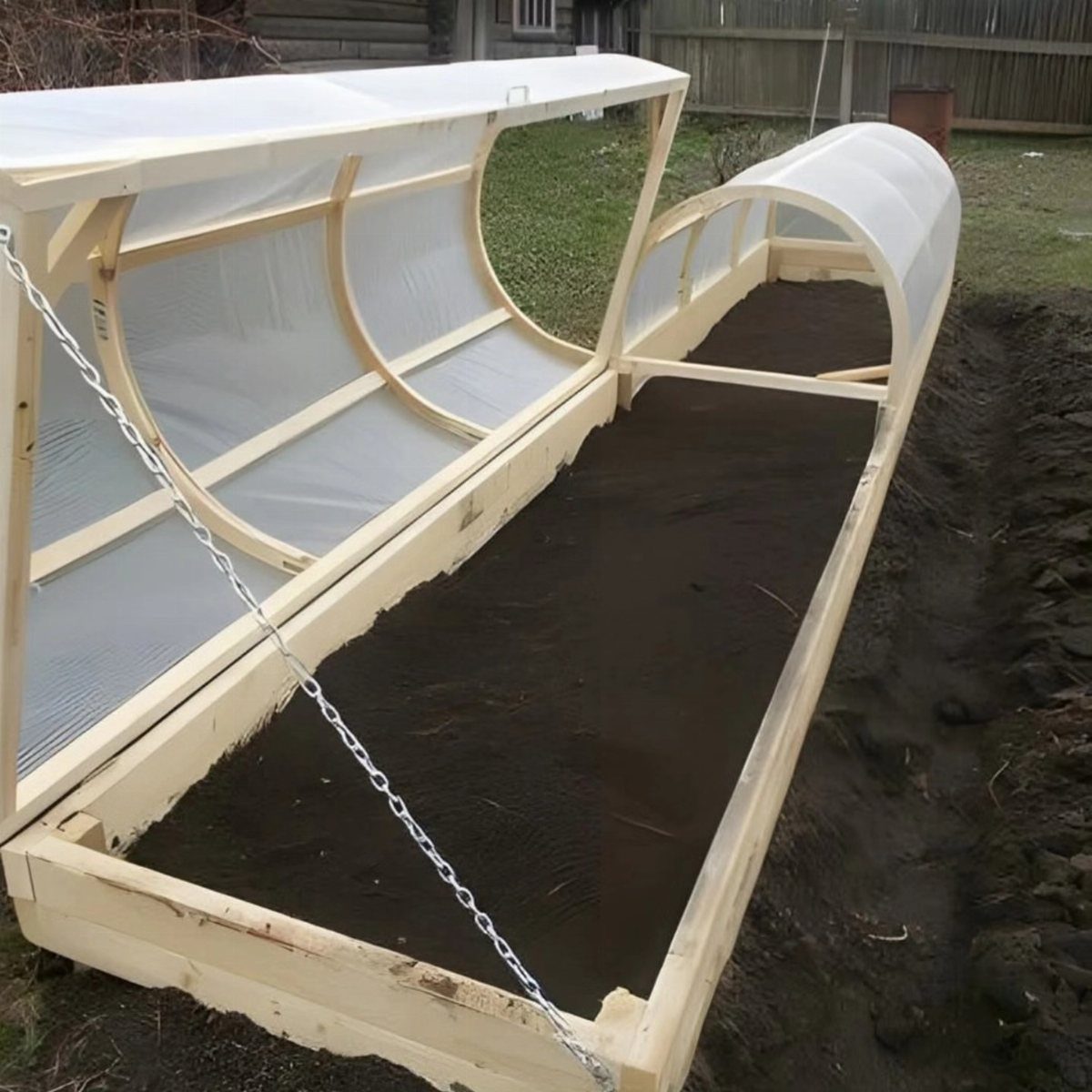 Easy Raised Garden: 9 Ideas for Any Budget and Skill Level 7 A long wooden raised garden bed with a translucent arched greenhouse cover filled with dark soil.