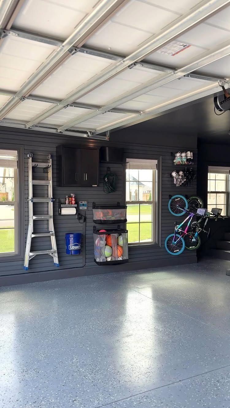 9 Garage Design Interior Ideas for Workspace, Storage and Style 1 Organized garage with dark grey walls, epoxy flooring, storage bins, and bicycles hanging on the wall.