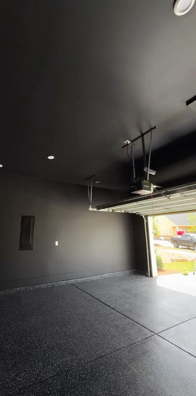 9 Garage Design Interior Ideas for Workspace, Storage and Style 8 A modern garage with black walls, a dark speckled epoxy floor, and an open garage door.