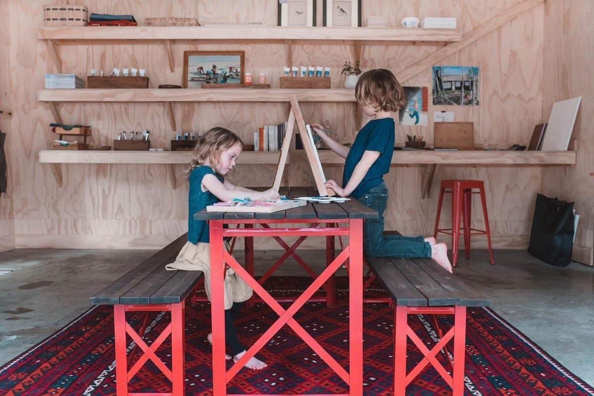 Garage to Family Room Conversion: 8 Ideas for 2026 7 Two children drawing at a red wooden table in a bright room with wooden shelves.
