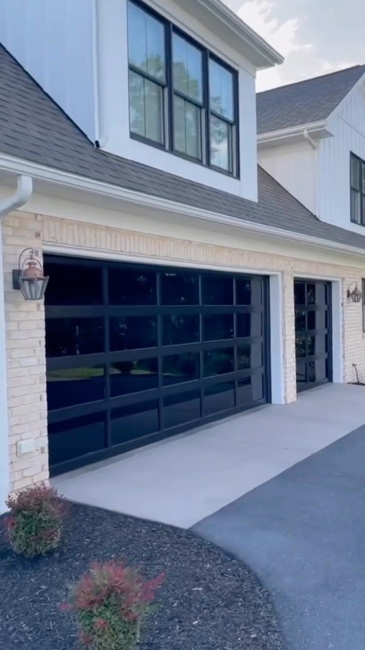 Garage to Family Room Conversion: 8 Ideas for 2026 1 White house with large black-framed glass garage doors and upper story windows.