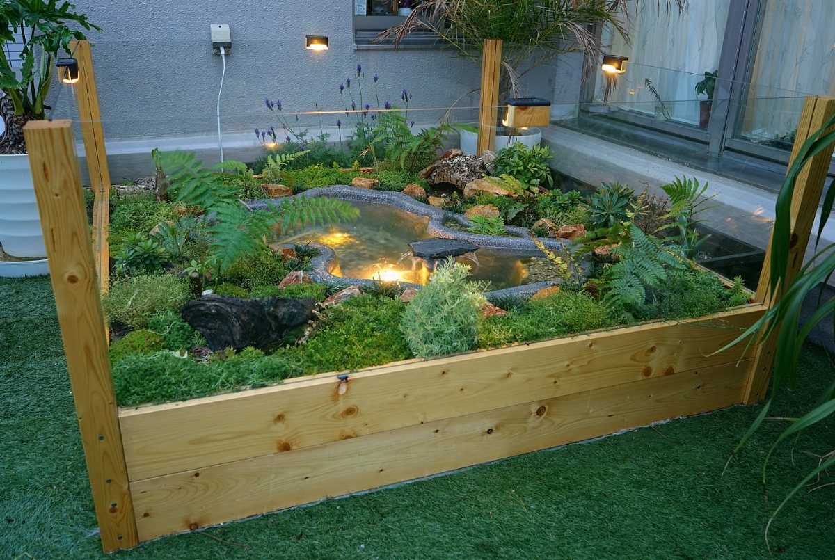 22 Backyard Garden Ideas for Patios, Beds, and Privacy 18 A small garden pond with lights and rocks nestled inside a wooden raised planter bed.