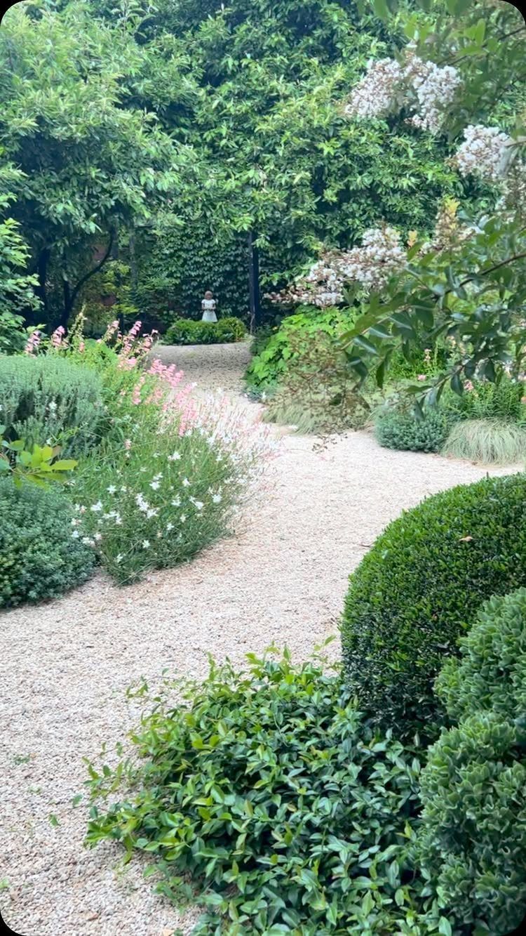 22 Backyard Garden Ideas for Patios, Beds, and Privacy 11 A winding gravel path curves through a lush garden filled with green shrubs and white flowers.