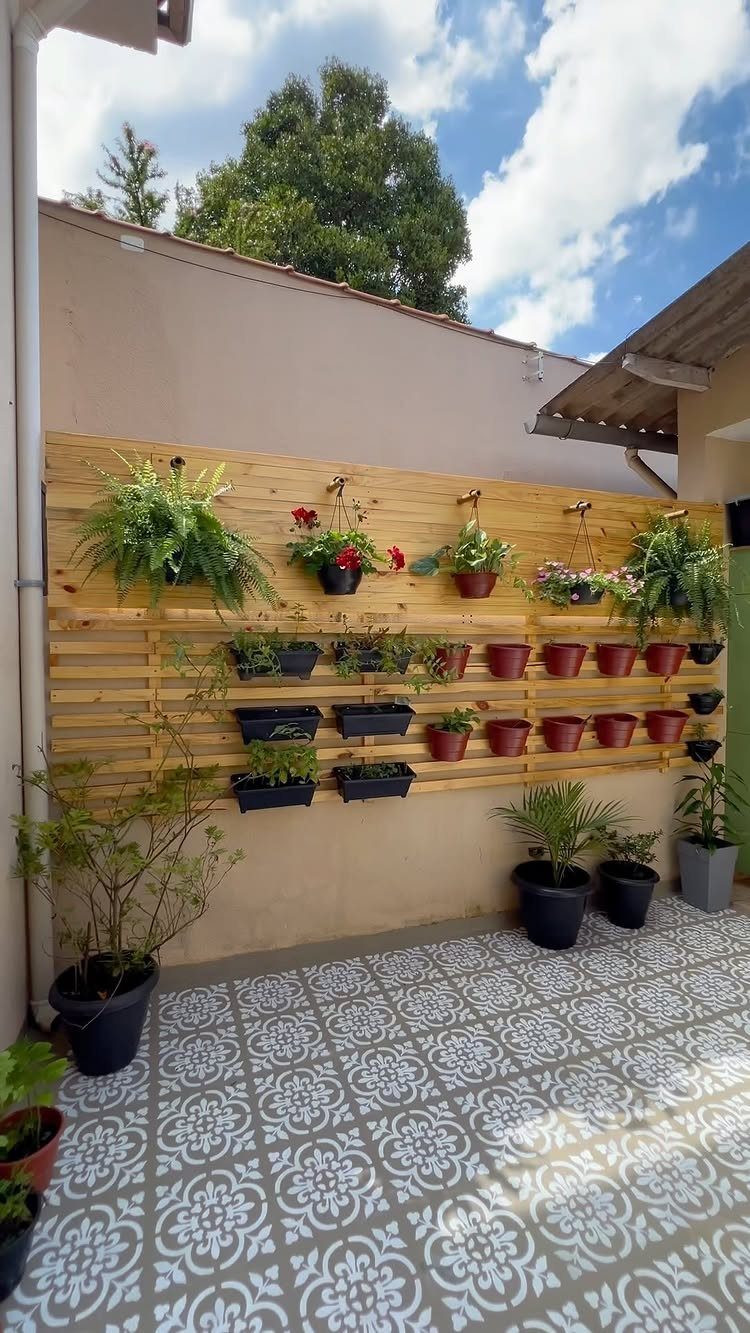 22 Backyard Garden Ideas for Patios, Beds, and Privacy 8 Wooden slat wall mounted with various potted plants and flowers on a tiled patio.