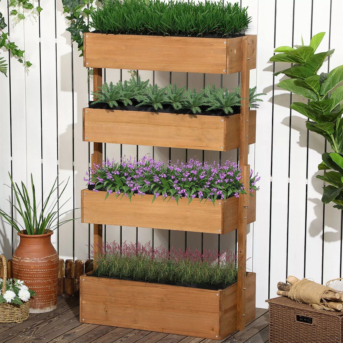 A four-tier wooden planter stand filled with green plants and purple flowers against a white wall.