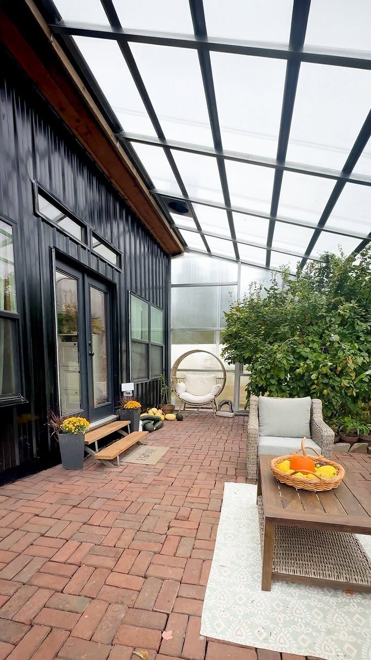 8 Houses With Greenhouses That Skip the Ordinary 7 A black house with glass doors leading to a brick patio under a large glass greenhouse roof structure.