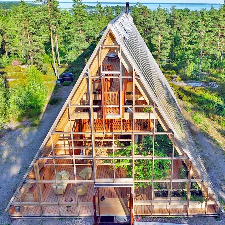 8 Houses With Greenhouses That Skip the Ordinary 1 A-frame house with a large integrated glass greenhouse structure surrounded by a lush green forest.