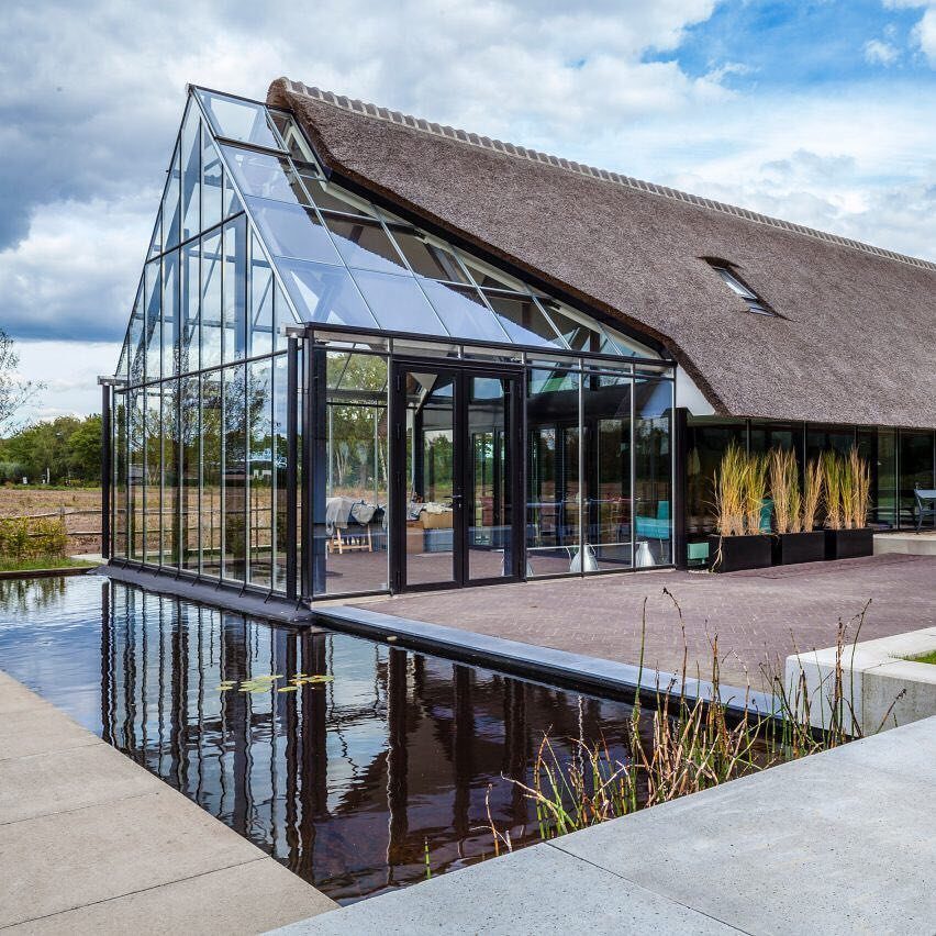 8 Houses With Greenhouses That Skip the Ordinary 8 A modern house with a large glass greenhouse attached to a thatched roof building.